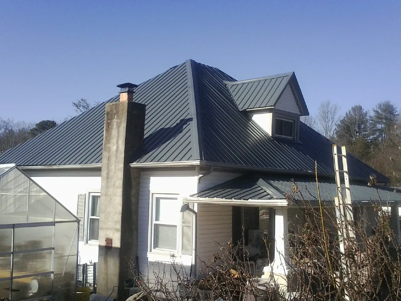 Dark blue standing seam metal roof on a white farmhouse with dormer — Slate & Tile Roof Repair by Roofing Brothers in Big Prairie