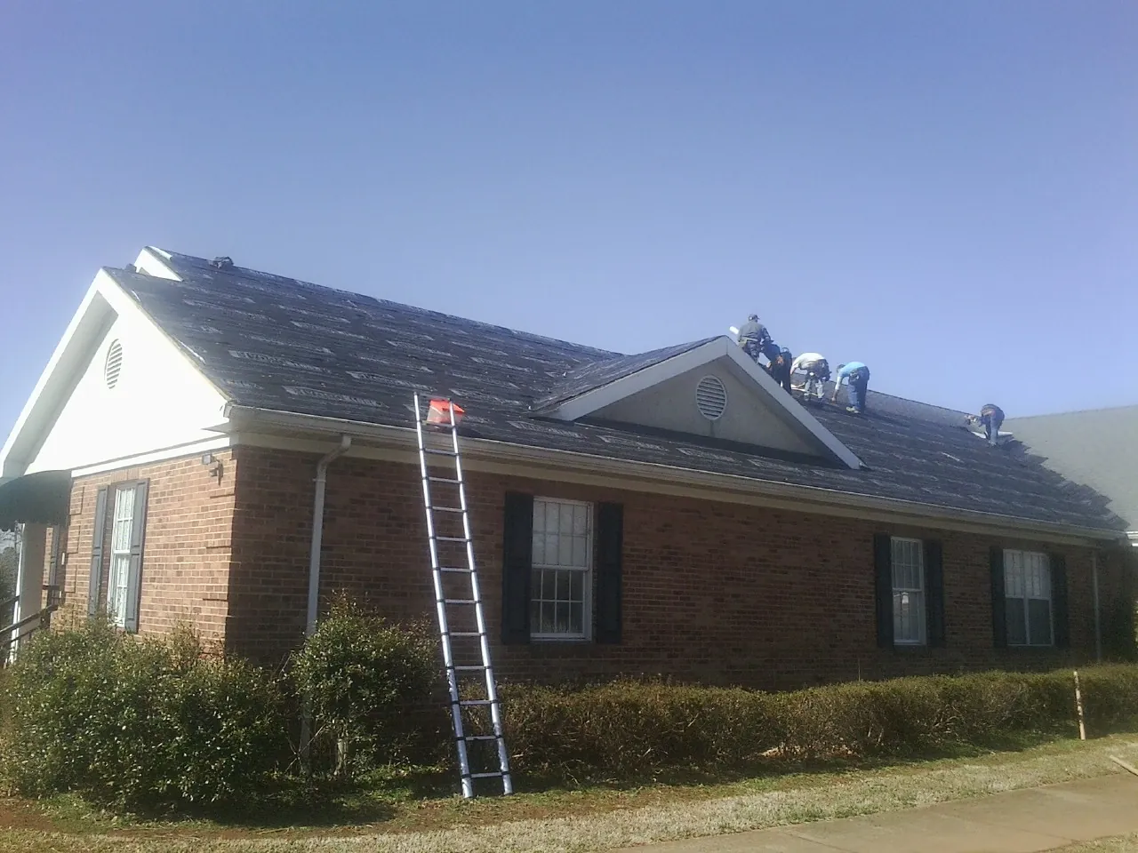 Crew tearing shingles off a brick ranch roof with a ladder set — Emergency Roof Repair work by our crew in Big Prairie