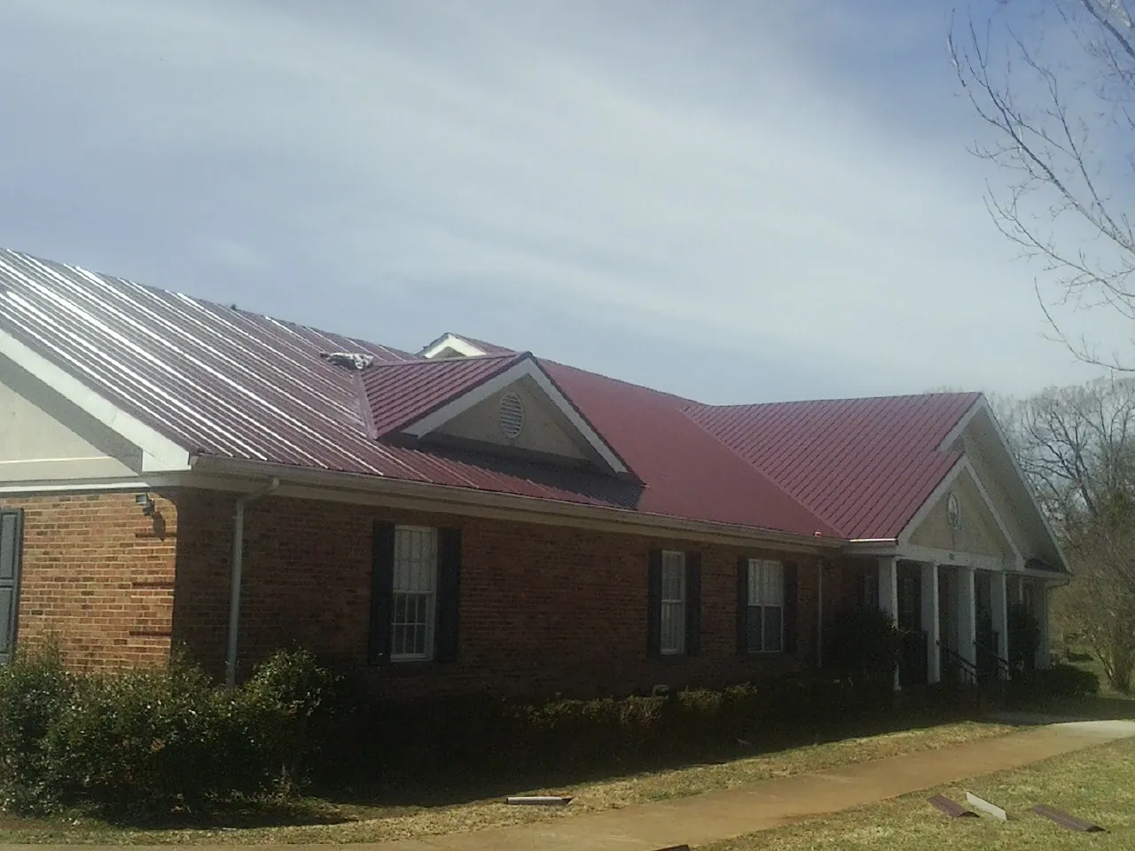 Red metal roof with gabled entries on a long brick building, from a Hail Damage Roof Repair job in Big Prairie