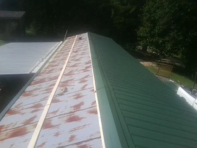 Old rusted panels beside newly installed green metal roofing — Wind Damage Roof Repair by Roofing Brothers in Big Prairie