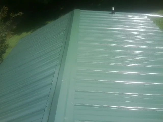 New green metal panels meeting at the ridge of a roof — Flat Roof Repair work by our crew in Big Prairie