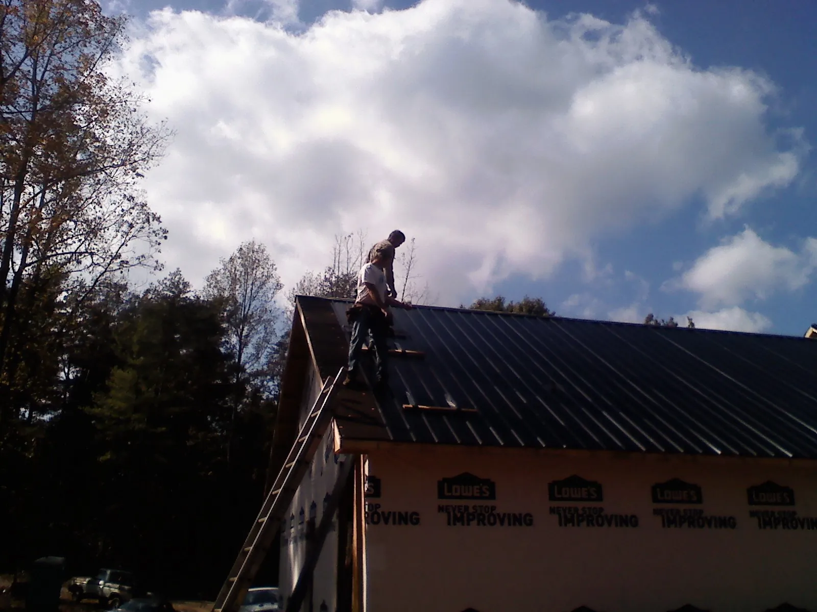 Roofer fastening dark metal panels high against a cloudy sky, from a Roof Inspection job in Big Prairie
