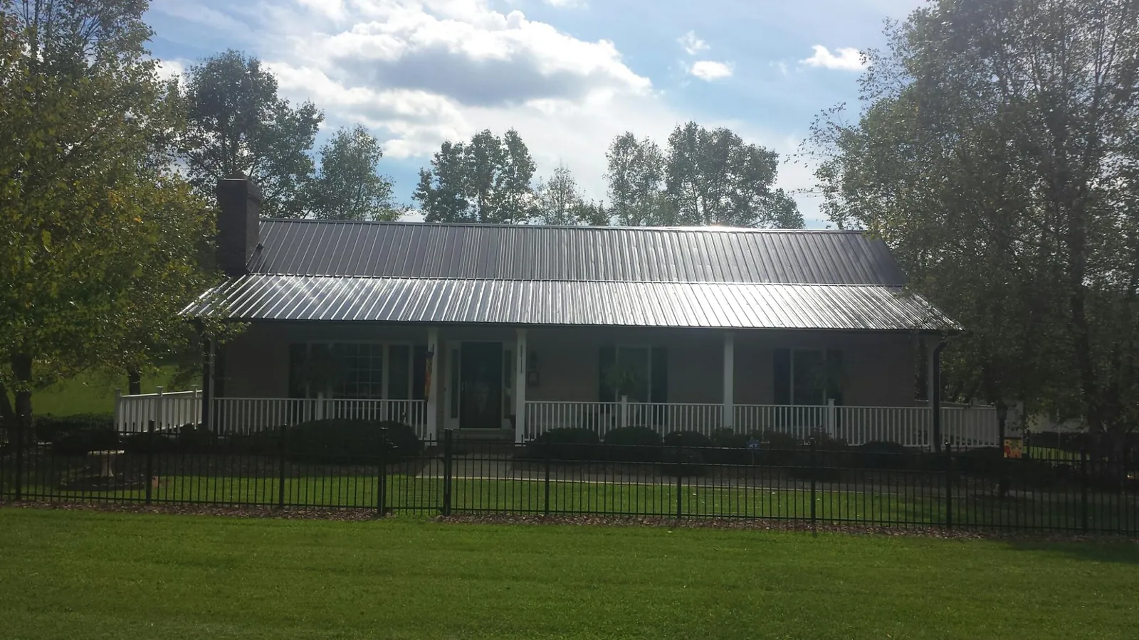 Gray metal roof on a brick ranch with a full width front porch — Gutter Guard Installation work by our crew in Big Prairie