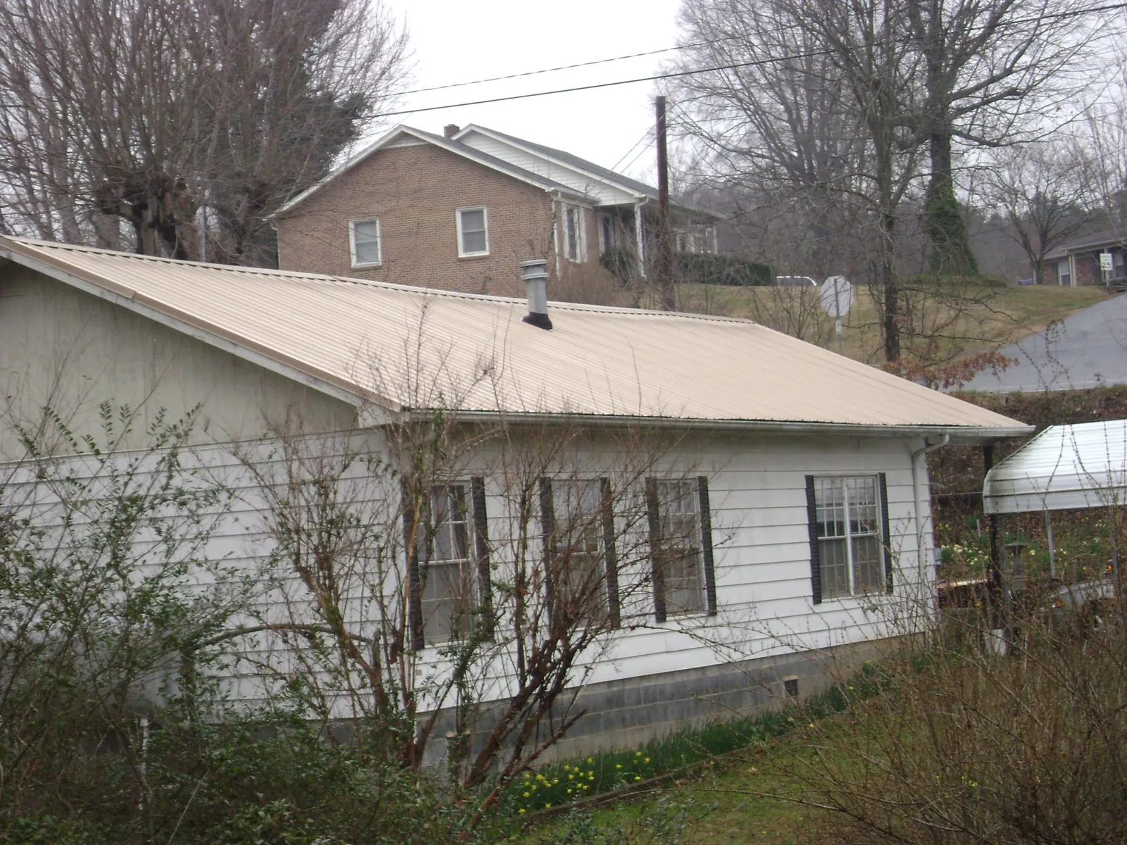 Tan metal roof on a white sided house set into a hillside — Commercial Roofing by Roofing Brothers in Big Prairie