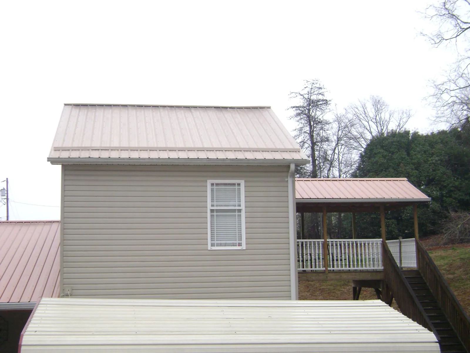 Tan metal roofs on a two story addition and attached porch, from a Roof Replacement job in Big Prairie